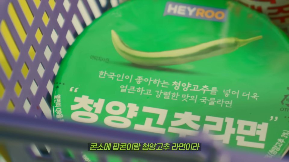 보라색 장바구니 안 초록색 컵라면 뚜껑에 HEYROO 로고와 「청양고추라면」 글자가 크게 보이고, 아래에 「콘소메 팝콘이랑 청양고추 라면이라」 자막이 뜬 장면