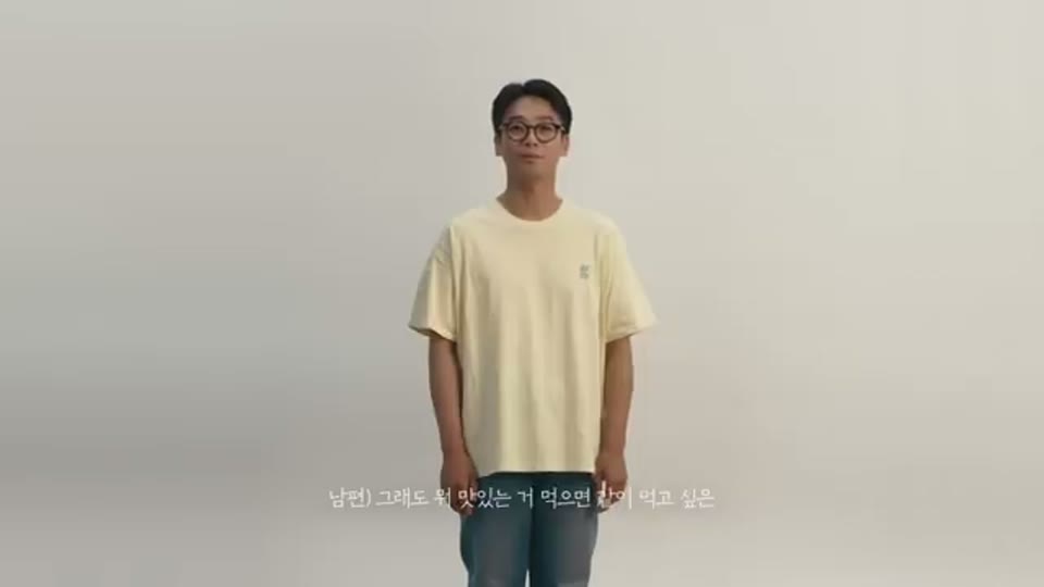 같은 회색 배경 앞에 반팔 티셔츠를 입은 남성이 정면을 보고 서 있고 하단에 자막이 붙은 장면