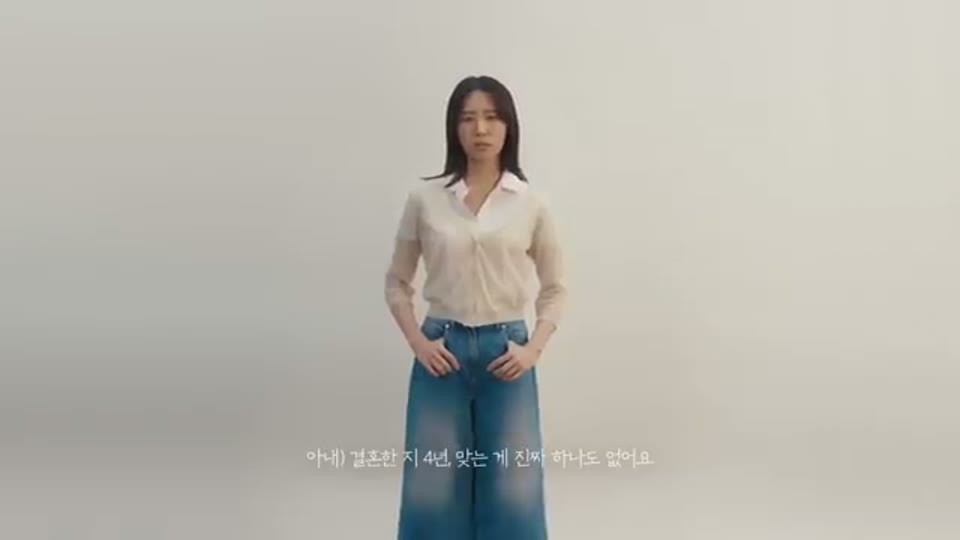 아무 배경 없는 밝은 회색 공간에 여성이 정면을 보고 서 있고 화면 하단에 화자를 표기한 자막이 붙은 장면