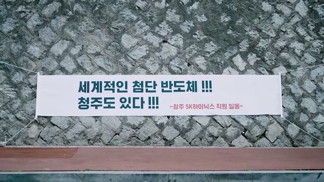 돌담 앞에 걸린 흰 현수막에 「세계적인 첨단 반도체!!! 청주도 있다!!!」와 「청주 SK하이닉스 직원 일동」이 적힌 장면
