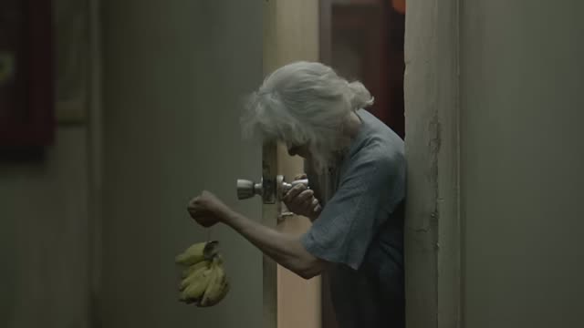 남자가 이웃 할머니 집 문손잡이에 바나나를 몰래 걸어 두는 장면